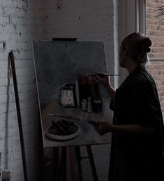 a woman is painting on an easel in front of a brick wall and window