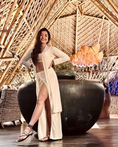 a woman posing for a photo in front of a bamboo structure with her legs crossed