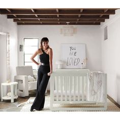 a woman standing next to a baby crib in a room with white furniture and decor