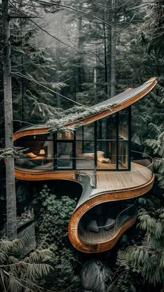 an unusual house in the woods surrounded by trees and rocks, with a curved wooden walkway leading up to it