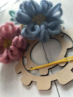 two yarn flowers sitting on top of a piece of wood