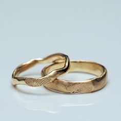 two gold wedding rings on a white surface with one ring in the shape of an elephant's tail