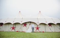 a bride and groom standing in front of a large tent with red stars on it