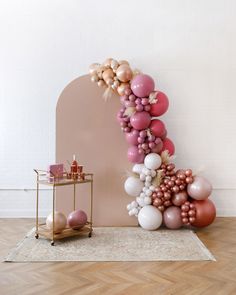 a balloon arch with pink, white and gold balloons on the floor next to it