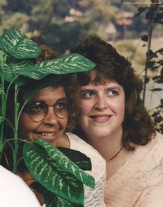 two women standing next to each other with green leaves on their heads and one has her arm around the woman's shoulder