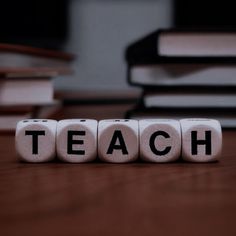 the word teach spelled out with dices on a wooden table in front of stacks of books