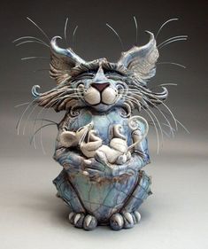 a ceramic sculpture of a cat with wings on its head and tail, sitting in front of a gray background