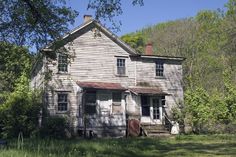 an old house in the woods with trees around it and grass on the ground below