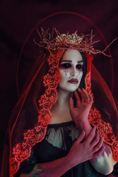 a woman with white makeup and red veil holding her hands to her face while wearing an elaborate head piece