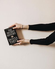 a woman holding a book in her hands on the floor next to a white wall