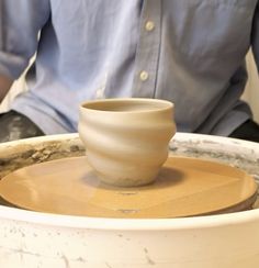 a man sitting at a table making a bowl on top of a potter's wheel