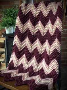 a crocheted blanket sitting on top of a wooden chair next to a potted plant