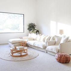 a living room filled with white furniture and a large window in the wall behind it