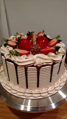 a cake with strawberries and chocolate icing on a metal platter sitting on a wooden table