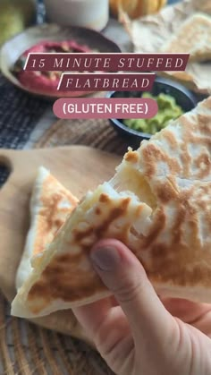 a hand holding a piece of flatbread with guacamole in the background