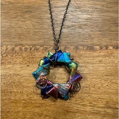 a multicolored necklace is hanging on a wooden table and it has a metal chain