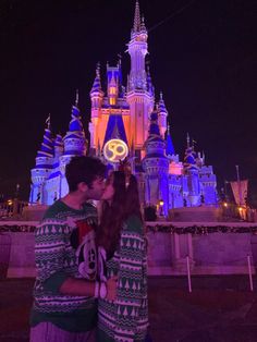 a man and woman kissing in front of a castle at night with the lights on