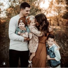 a man, woman and two children are posing for a family photo in the woods