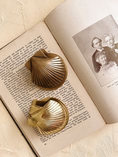 an open book with two gold seashells sitting on it's side next to each other