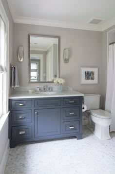 a white toilet sitting under a bathroom mirror next to a sink in a room with gray walls