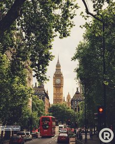 a red double decker bus driving down a street next to tall buildings with a clock tower in the background