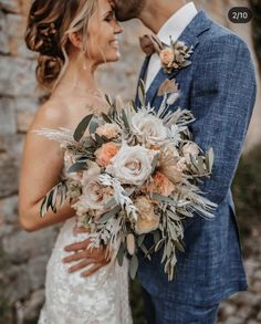 a bride and groom standing next to each other in front of a stone wall with flowers