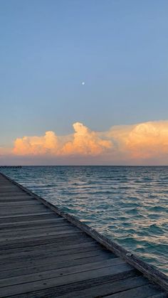 a long pier stretching out into the ocean at sunset with clouds in the sky above