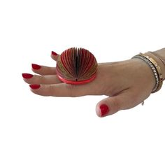 a woman's hand holding a red and gold ring with a fan on it