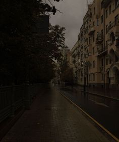 an empty city street in the rain with buildings on either side and one person walking down the sidewalk