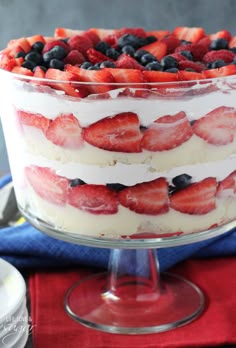 a trifle with strawberries and blueberries in it on a glass cake stand