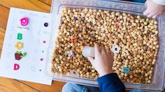 a child is playing with some food in a plastic container on the floor next to other children's hands