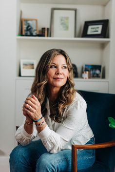 a woman sitting on top of a blue chair in front of a book shelf with books