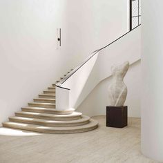 a sculpture sitting on top of a wooden stand next to a stair case in a white room