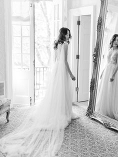 a woman standing in front of a mirror wearing a wedding dress and looking at herself in the mirror