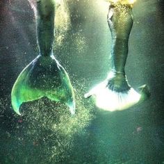 two mermaids are swimming in the water with their tails spread out and feet up