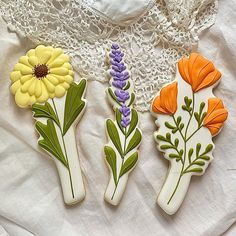 three decorated cookies sitting on top of a white cloth covered table next to a lace doily