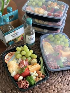 three plastic containers filled with food on top of a wicker table next to bottles of water