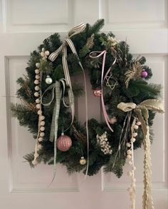 a wreath hanging on the front door decorated with christmas ornaments and ribbons, along with other holiday decorations