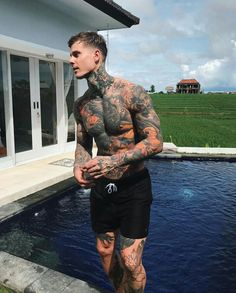 a tattooed man standing in front of a swimming pool with his hands on his hips