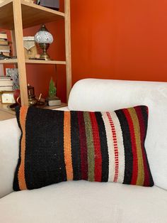 a white couch with a colorful striped pillow on it's back in front of an orange wall