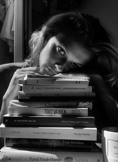 a woman leaning her head on a stack of books