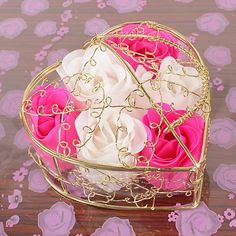 pink and white flowers are in a heart shaped container on a table with purple petals