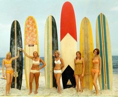 four women in bathing suits standing next to surfboards on the sand at the beach