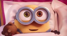 a minion with big eyes sitting in bed next to a teddy bear and stuffed animal