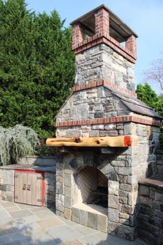 an outdoor brick pizza oven in the middle of a patio with trees and bushes behind it