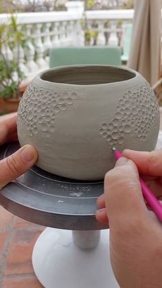 a person is working on a vase with a marker in their left hand and the other hand holding it