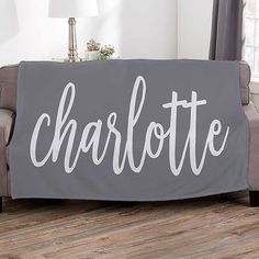 a couch with a blanket that says charlotte on it in white letters, sitting next to a lamp