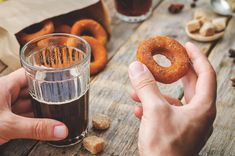 a person holding a doughnut next to a cup of coffee on a wooden table