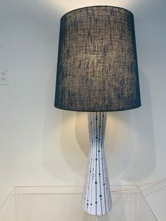 a lamp that is sitting on top of a glass table with a black and white shade