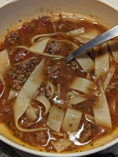 a white bowl filled with pasta and meat soup on top of a black table cloth